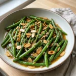 A close-up of tender green beans topped with chopped toasted almonds and a light sauce.