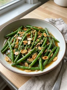 A close-up of tender green beans topped with chopped toasted almonds and a light sauce.