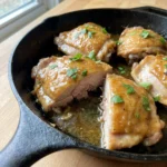 A serving of cider glazed chicken thighs next to a scoop of mashed potatoes.